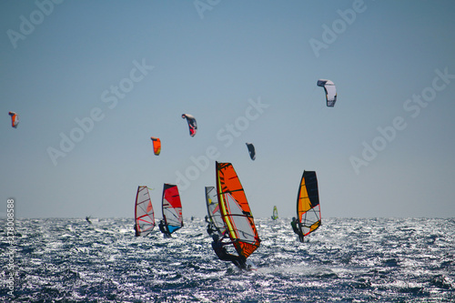 Fototapety Windsurfing  windsurferzy-i-kiteboarderzy-na-wzburzonym-morzu-w-podswietleniu