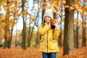 Poster - childhood, season and people concept - happy girl with pumpkin at autumn park