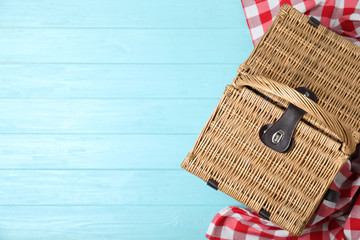 Closed wicker picnic basket and checkered blanket on wooden table, top view. Space for text