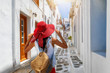 Weibliche Touristin mit rotem Hut erkundet die kleinen, weißen Gassen von Mykonos Stadt während ihres Sommerurlaubes in Griechenland