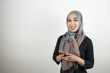 young attractive smiling Muslim woman wearing turban hijab headscarf holding smartphone in her hands isolated white background