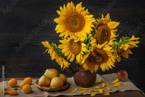 Fotografía Still life with sunflowers in a clay pot and fruit on against a wooden wall