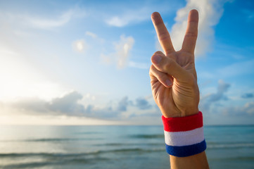 American athlete wearing USA colors red, white, and blue wristband holding peace sign fingers against blue sky