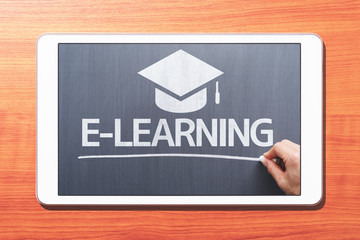 Aufkleber - E-learning concept. Tablet computer on wooden desk. Teacher writing on blackboard. Front view image.