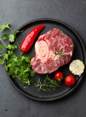 Wall Mural - Raw fresh ossobuco con herbs, garlic and chile pepper on black plate. Dark background