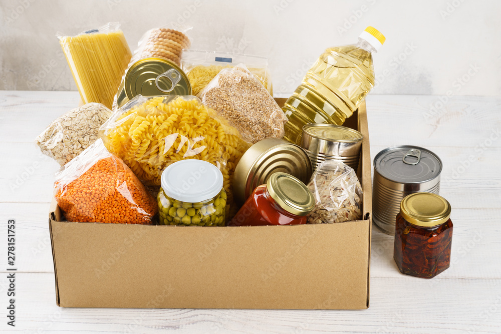 Various canned food, pasta and cereals in a cardboard box. - obrazy, fototapety, plakaty 