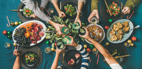 Company of friends of different ages gathering for Christmas or New Year party dinner at festive table. Flat-lay of hands holding glasses with drinks, feasting and celebrating holiday, top view