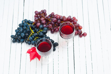 two glasses of red wine and grapes on white wooden table background