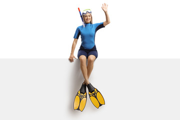 Poster - Young woman in a wetsuit, a diving mask and flippers sitting on a banner and waving