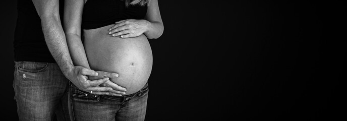 pregnant belly couple holding hands around baby bump black background