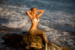 beautiful mermaid with golden tail sits on the seashore