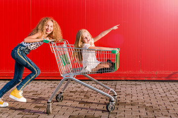 2 girls having fun and having fun with a grocery cart against the background of a red wall