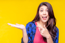 Beautiful Young Asian Woman Pointing Finger To Copy Space. Attractive Beautiful Girl Show Product That Make Her Satisfied, Excited, Love, Surprise With Exciting Face, Surprise Face. Yellow Background