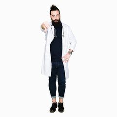 Wall Mural - Doctor with long hair wearing medical coat and stethoscope looking unhappy and angry showing rejection and negative with thumbs down gesture. Bad expression.