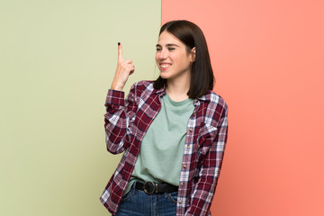 Wall Mural - Young woman over isolated colorful wall showing and lifting a finger in sign of the best