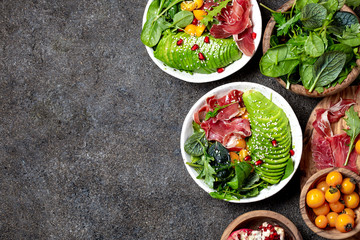 Wall Mural - Low carbs bowl. Fresh salad with green spinach, rucola, avocado an ham serrano in white bowl, gray background, top view