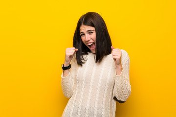 Wall Mural - Young woman over isolated yellow wall celebrating a victory in winner position