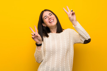 Wall Mural - Young woman over isolated yellow wall showing victory sign with both hands