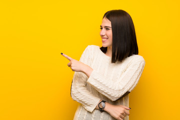 Wall Mural - Young woman over isolated yellow wall pointing to the side to present a product