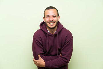 Wall Mural - Colombian man with sweatshirt over green wall laughing