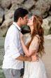 © FrameSculptor - Bride and groom are hugging on the beach against the backdrop of rocks. Young couple bowed to each other before a kiss. Newlyweds at wedding day on ocean beach