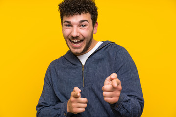 Young man over isolated yellow wall points finger at you