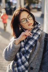 Wall Mural - Attractive young girl wearing glasses in a coat walking on a sunny day