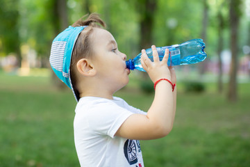 a little boy drinks mineral water from a plastic bottle in the Park in the summer