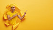 Pleased cheerful man attracts your attention to special offer, points at upper right corner, poses in torn paper hole of yellow background. People, promotion concept. Satisfied guy promots object