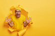 © WHstudio Leushin N - Emotional unshaven guy stands in ripped paper hole of yellow background, yells loudly, gestures and shows palms, tries to prevent you from danger, shouts be carefully, wears bright hat and t shirt