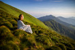 © Serhii - Young woman sitting on a rock and looking to the horizon. Happy traveler enjoying sunset view. Girl in long white dress in the mountains
