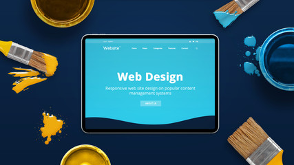 Leinwandbilder - Modern tablet on a blue desk with creative flat design theme od web design studio. Concept of creating modern web sites. Color brushes and boxes beside.