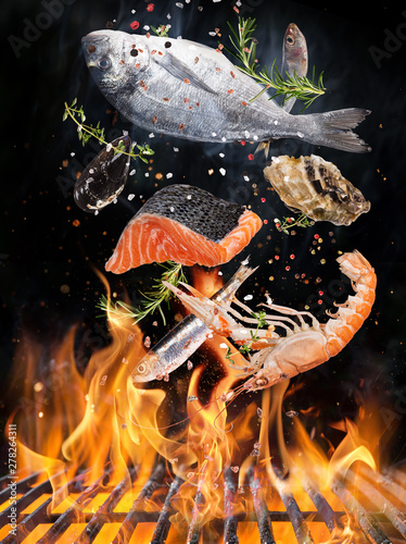 Fotografía Kettle grill with fire flames, cast iron grate and tasty sea fishes flying in the air
