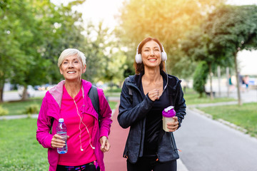 Happy mother and daughter jogging together outdoors in park.