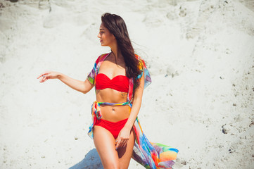 Amazing girl with sexy body is engaged in fitness on the white sand beach. Young women in swimsuit sunbathing on a summer vacation abroad. Charming model on a desert island.