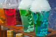 Multicolored fruit drinks close-up. Non-alcoholic drinks in plastic cups at the festival. Cocktails with juice and greens. White smoke is steaming with cocktails.