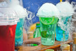 Multicolored fruit drinks close-up. Non-alcoholic drinks in plastic cups at the festival. Cocktails with juice and greens. White smoke is steaming with cocktails.