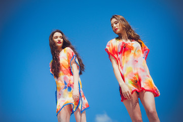 Two gorgeous young women wearing swimmwear, against the blue sky