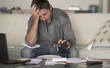 © TheVisualsYouNeed - stressed and desperate man at home living room couch doing domestic accounting with paperwork and calculator feeling overwhelmed and worried suffering financial crisis