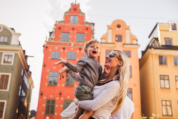 Portrait of the happy young mother who is standing outdoors and holding her cute little son in arms