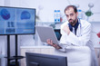 © DC Studio - Young bearded doctor looking at the camera and holding a laptop