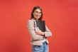 Young smiling student or intern in eyeglasses standing with a folder on red background.