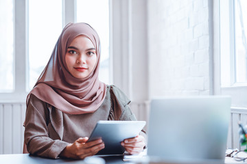 Happy Arabic business woman in brown hijab working with tablet and laptop at office workplace.