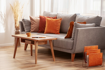 living room with wooden coffee table and grey couch with ginger, orange and red pillows