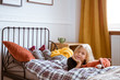 Smiling kid laying in her bed on the checkered flannel bedclothes in white bedroom