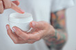 © Artem Markin - Female tattooed hands holding a jar of cream. Finger with a drop of white cream