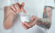 © Artem Markin - Female tattooed hands holding a jar of cream. Finger with a drop of white cream