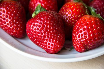 Fresh strawberries on a white plate on a wooden light background, copy space. Strawberry background. Sweet, juicy, ripe strawberries. Harvest of organic local  strawberries. Healthy food with vitamins