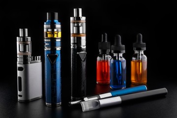 Wall Mural - Electronic cigarettes and bottles with vape liquid on black background