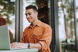© Yakobchuk Olena - Joyful young man in orange shirt using laptop